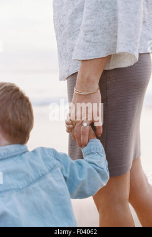 Femme debout sur une plage de sable fin à l'océan, tenant la main de son jeune fils. Banque D'Images