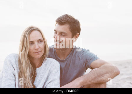 Un couple assis sur une plage, un homme et une femme avec leurs bras autour de l'autre et chefs ensemble. Banque D'Images