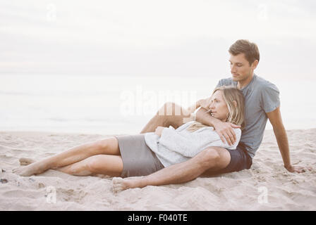 Un couple assis sur une plage, un homme et une femme avec leurs bras autour de l'autre et chefs ensemble. Banque D'Images