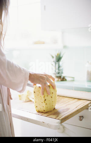 Femme debout dans une cuisine, découpage d'un ananas frais.