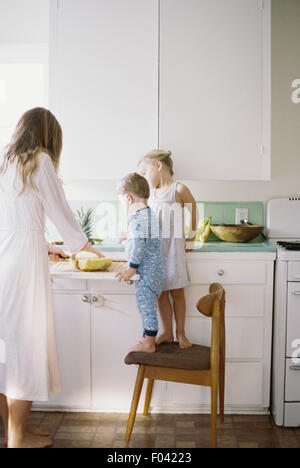 Femme debout dans une cuisine, découpage d'un ananas frais pour ses enfants. Banque D'Images