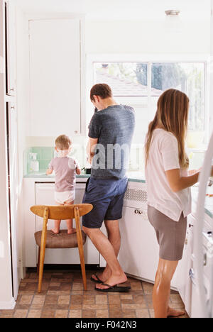 Couple standing dans une cuisine, leur fils debout sur une chaise à côté d'eux. Banque D'Images