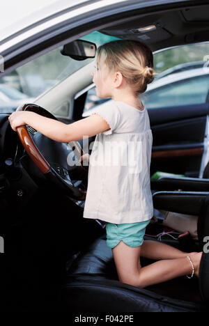 Jeune fille à genoux sur le siège du conducteur d'une voiture, maintenant la roue, en faisant semblant de conduire. Banque D'Images