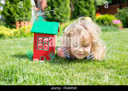 Maquette en bois de la maison et de la petite fille blonde allongée sur l'herbe verte. Concept immobilier Banque D'Images