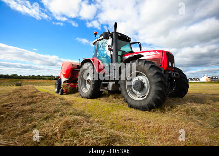 Tracteur énorme botte de collecte dans le domaine dans une belle journée ensoleillée bleu Banque D'Images
