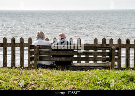 Couple de personnes âgées assis sur banc en bois face à la mer Banque D'Images