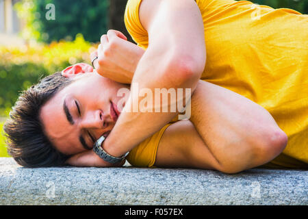 Beau jeune homme dormir sur banc en pierre en plein air parc de la ville pendant la journée Banque D'Images