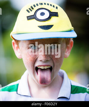 Jeune garçon avec des taches de rousseur et portant un chapeau de minion colle sa langue sur l'appareil photo Banque D'Images