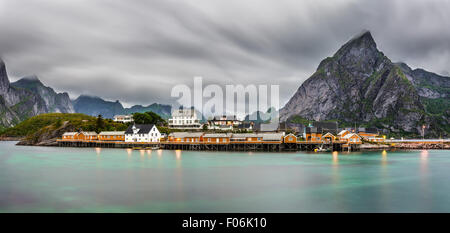 Panorama du mont Olstind au-dessus des cabines jaunes et jaunes eaux de Sakrisoy village de pêcheurs sur les îles Lofoten en Norvège. Banque D'Images