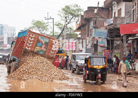 La pluie torrentielle résultats dans un village indien de l'unsurfaced road croulant sous un camion, ce qui le fait chavirer et jette sa charge Banque D'Images