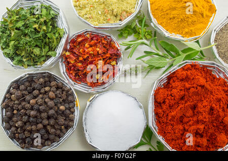 Épices diverses dans des bols brillants avec des plantes fraîches sur une table en bois blanc, Close up Banque D'Images