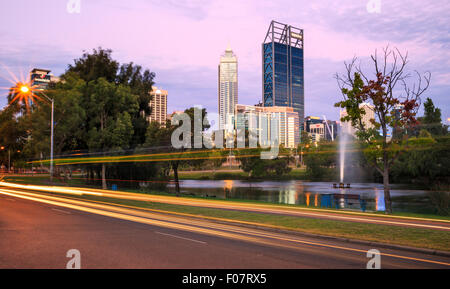 Les phares de voitures filant le long de la route au coucher du soleil avec la ville de Perth en arrière-plan. Banque D'Images