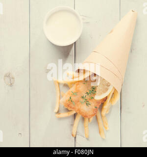 Fish and chips. Vue de dessus le filet de poisson frit avec des frites enveloppés par membrane en papier, sur un parquet en bois dans l'arrière-plan vintage tone. Banque D'Images