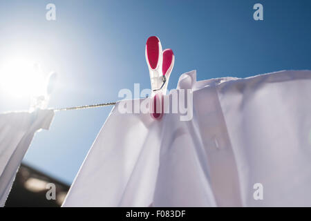 Blanchisserie rouge et blanc séchant au soleil fixé sur la ligne de lavage avec chevilles de couleur. Banque D'Images