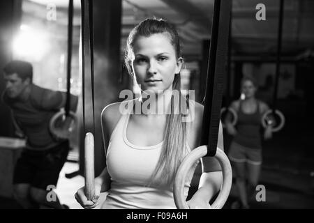 Tourné en noir et blanc d'une femme à l'aide d'anneaux de gymnastique en salle de sport Banque D'Images