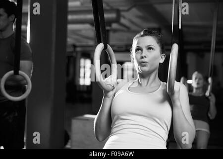 Tourné en noir et blanc d'une femme à l'aide d'anneaux de gymnastique en salle de sport Banque D'Images