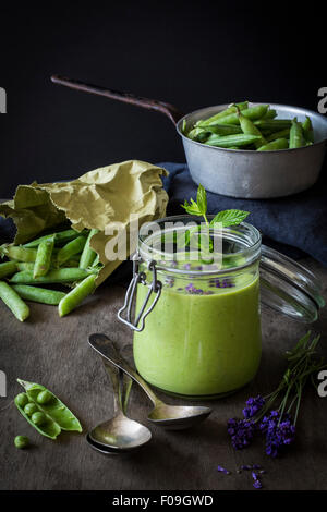 Gaspacho vert en pot avec des petits pois et de lavande sur table en bois avec une passoire et cuillères vintage Banque D'Images