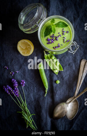 Gaspacho vert en pot avec des petits pois et de lavande sur fond gris avec serviette vintage cuillères. Vue d'en haut