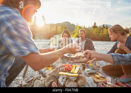 Les adultes assis autour de camp servant de la nourriture d'un barbecue Banque D'Images