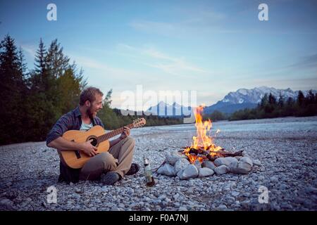 Jeune homme assis par camp à jouer de la guitare, chant, Wallgau, Bavière, Allemagne Banque D'Images