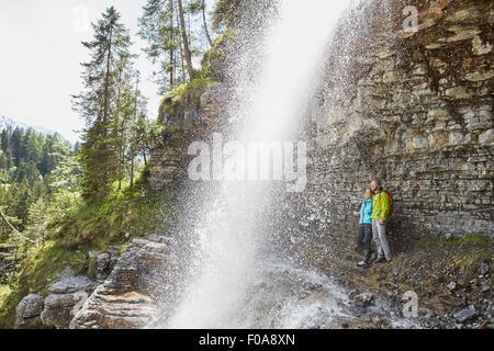 Jeune couple debout sous une cascade, looking out, Tyrol, Autriche Banque D'Images