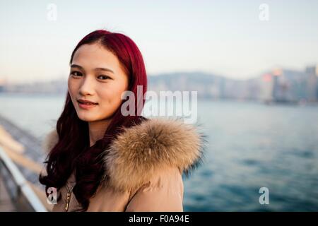 Portrait of young woman wearing fur trim manteau avec les cheveux teints en rouge en face de l'eau Banque D'Images