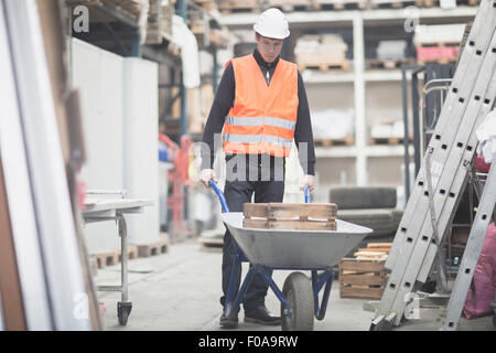 Young male warehouse worker pushing wheelbarrow in warehouse Banque D'Images