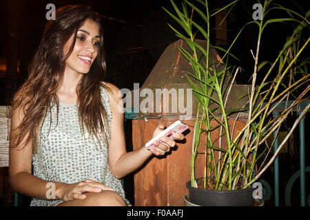 Jeune femme assise à l'extérieur la nuit, holding smartphone Banque D'Images