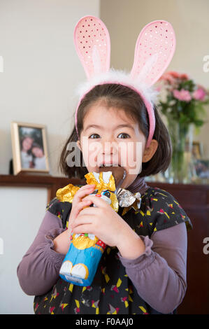 Young Girl wearing bunny ears, juste au sujet de mordre dans chocolate bunny Banque D'Images