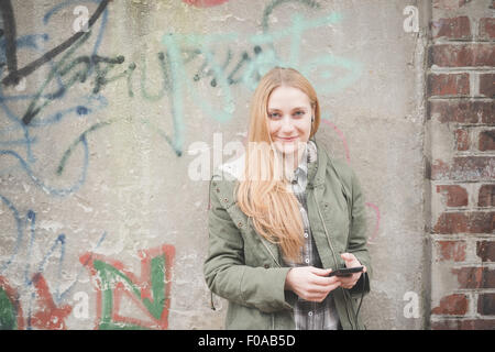Young woman using smartphone par mur de graffiti Banque D'Images