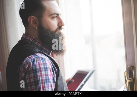 Jeune homme barbu using digital tablet in room Banque D'Images