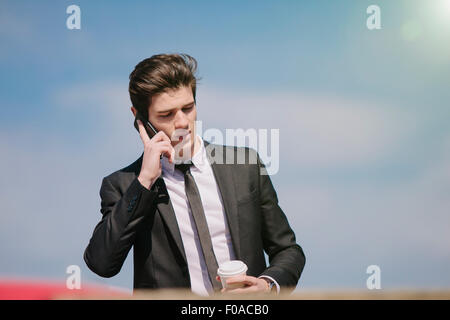 Young businessman chatting on smartphone alors que boire du café à emporter Banque D'Images