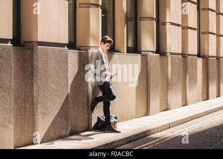 Ville jeune businessman leaning against office building lecture texte smartphone Banque D'Images