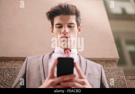 Low angle view of young businessman reading ville texte smartphone Banque D'Images