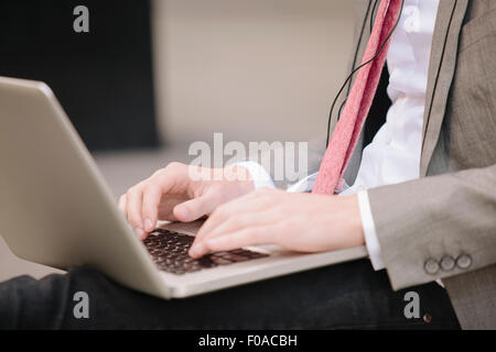 Cropped shot of young businessman sitting on ville trottoir typing on laptop Banque D'Images