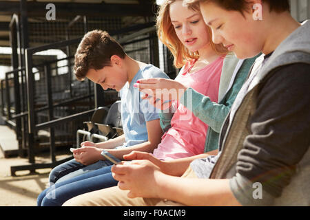 Quatre garçons et filles, la lecture de textes en stand stade smartphone Banque D'Images