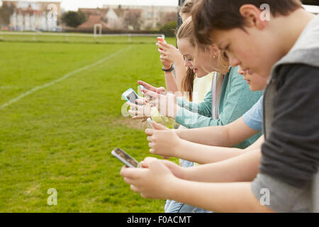 Rangée de cinq garçons et filles, la lecture des messages texte smartphone au terrain de football Banque D'Images