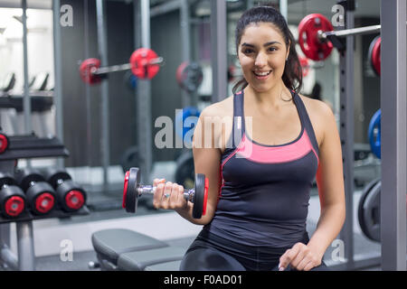 Portrait of a smiling young woman at gym holding dumbbell Banque D'Images