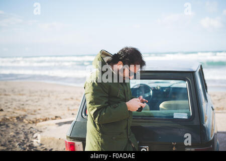 Homme avec vintage car sur la plage, lecture des textes smartphone Sorso, Sassari, Sardaigne, Italie Banque D'Images