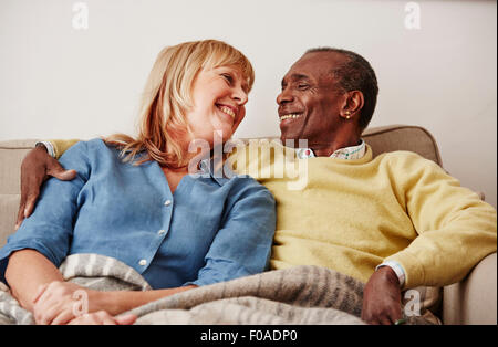 Couple sitting on sofa, smiling Banque D'Images