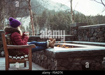 Jeune femme assise sur un banc de travail avec feu de camp, Girdwood, Alaska, Anchorage Banque D'Images