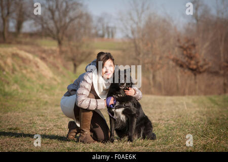 Portrait of mid adult woman kneeling with her dog in field Banque D'Images