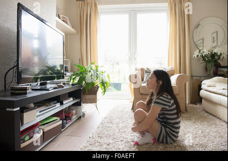 Fille assise sur le tapis à regarder la télévision Banque D'Images