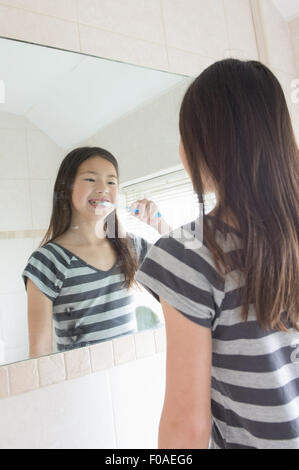 Jeune fille se brosser les dents en miroir de salle de bains Banque D'Images