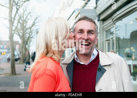 Woman kissing boyfriend on joue sur village street Banque D'Images