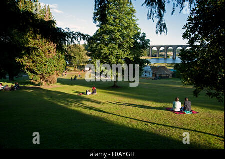 Festivaliers lounge sur l'herbe des pelouses par l'estuaire et viaduc au coucher du soleil au Port Eliot Cornwall Festival Banque D'Images