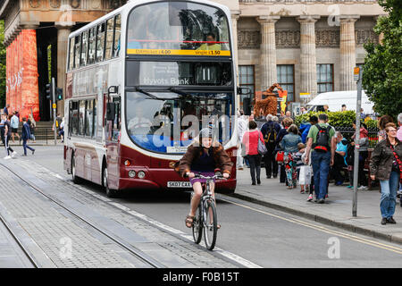 Femme vélo dans la voie de circulation limitée aux bus, trams et cyclistes suivis d'un double bus Decker, Princes Street, Banque D'Images