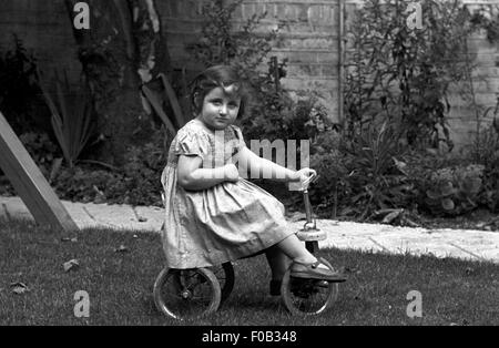 Une jeune fille sur son tricycle dans le jardin Banque D'Images