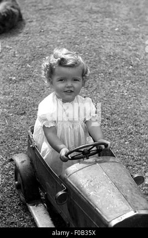 Une petite fille dans un jouet voiture d'étain en souriant. Banque D'Images