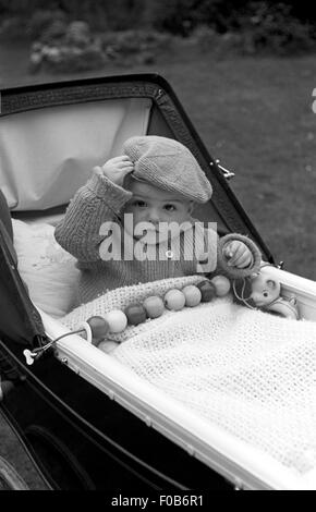 Un bébé portant un béret et laineux tricoté cardigan, assis dans une poussette. Banque D'Images